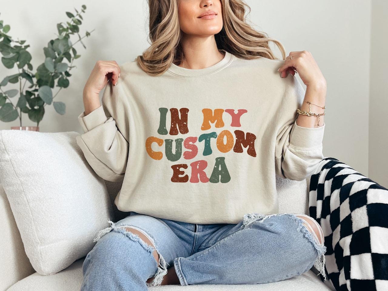 a woman sitting on a couch holding up a sweatshirt