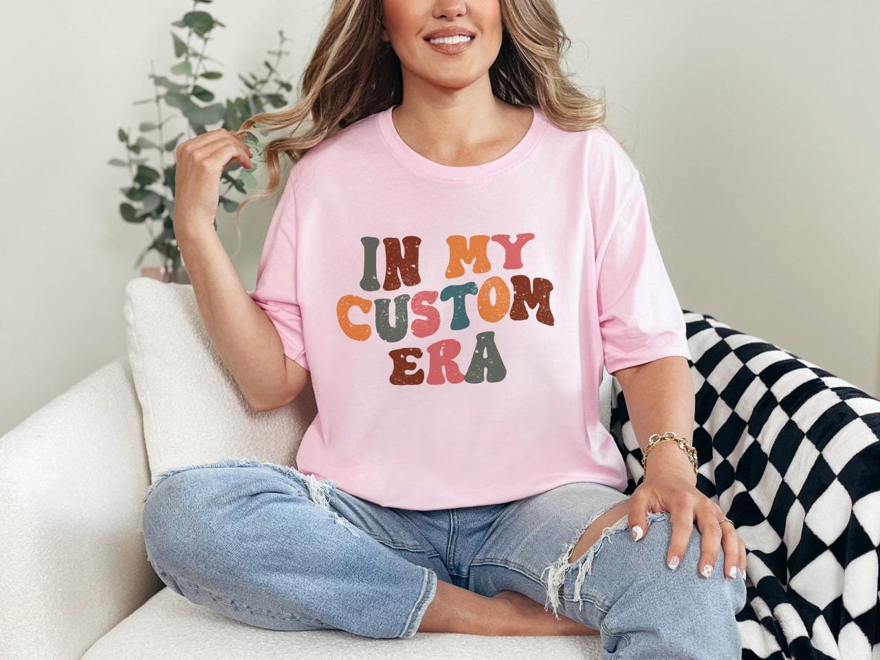 a woman sitting on a couch wearing a pink shirt that says in my custom era