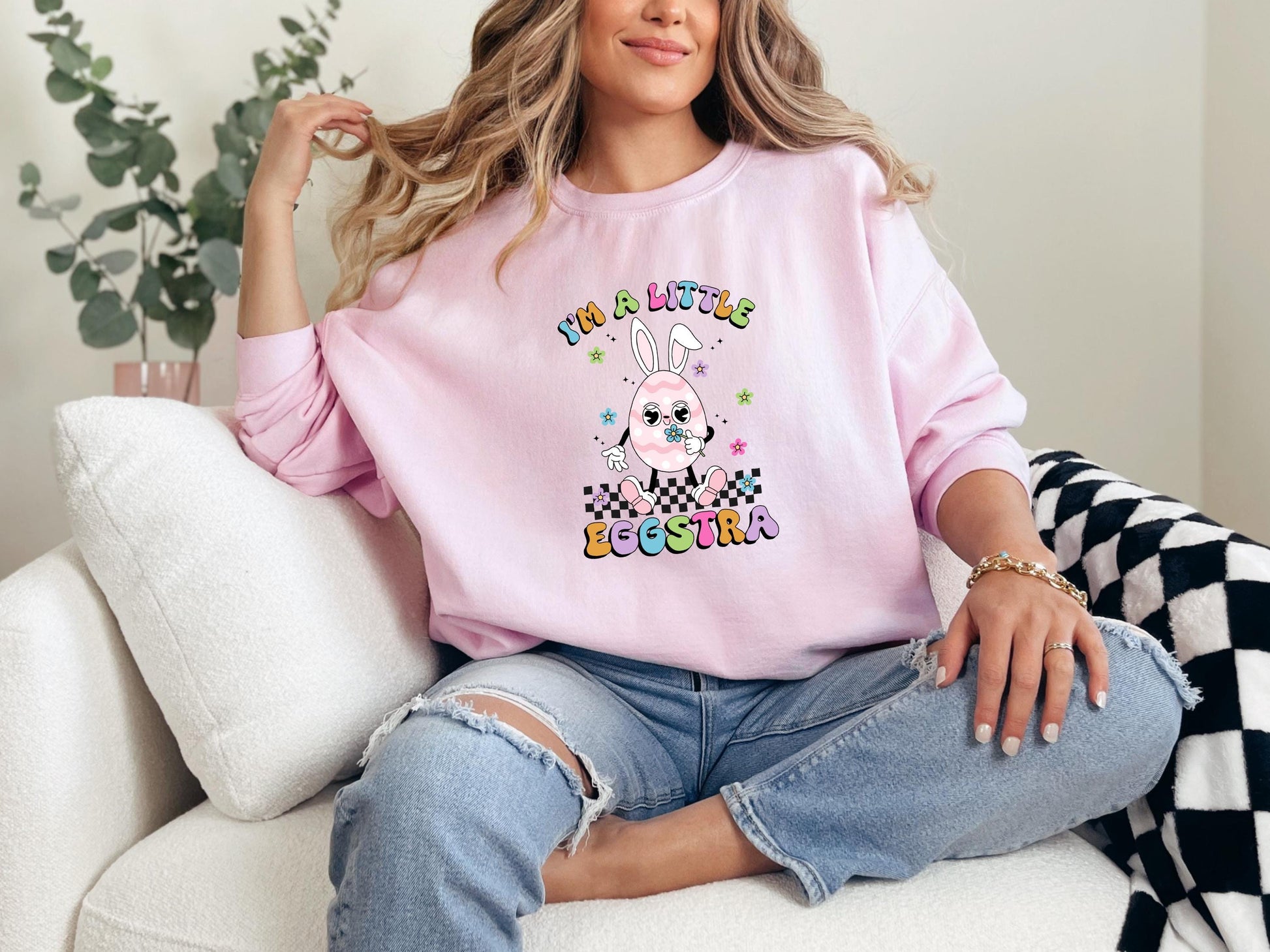 a woman sitting on a couch wearing a pink sweatshirt