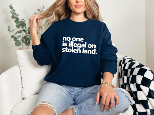 a woman sitting on a couch wearing a sweatshirt that says no one is illegal on