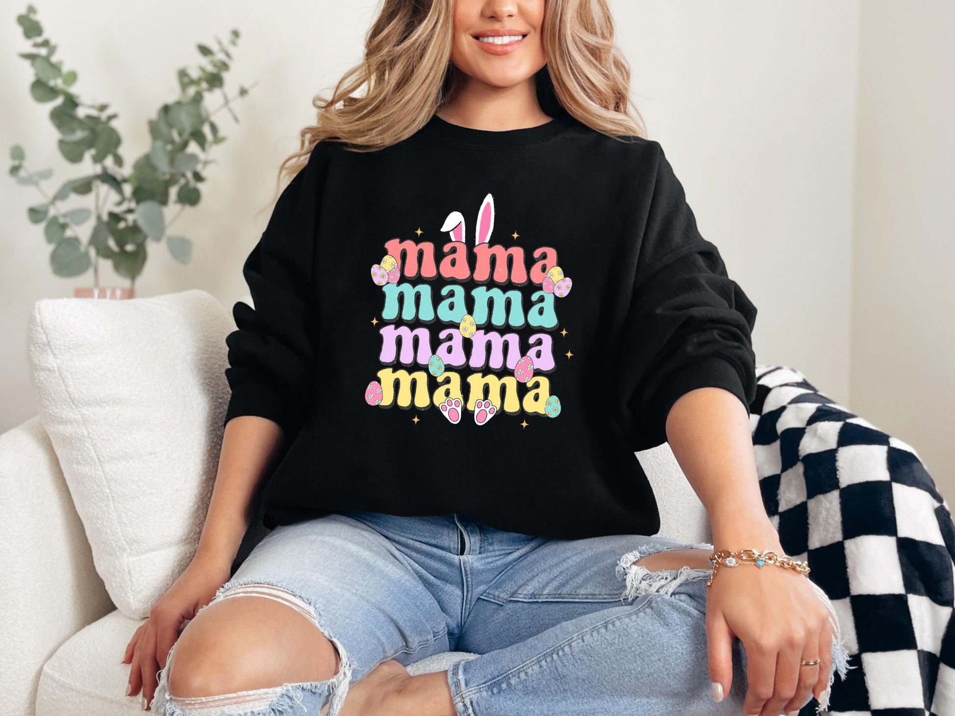 a woman sitting on a couch wearing a black mama mama sweatshirt