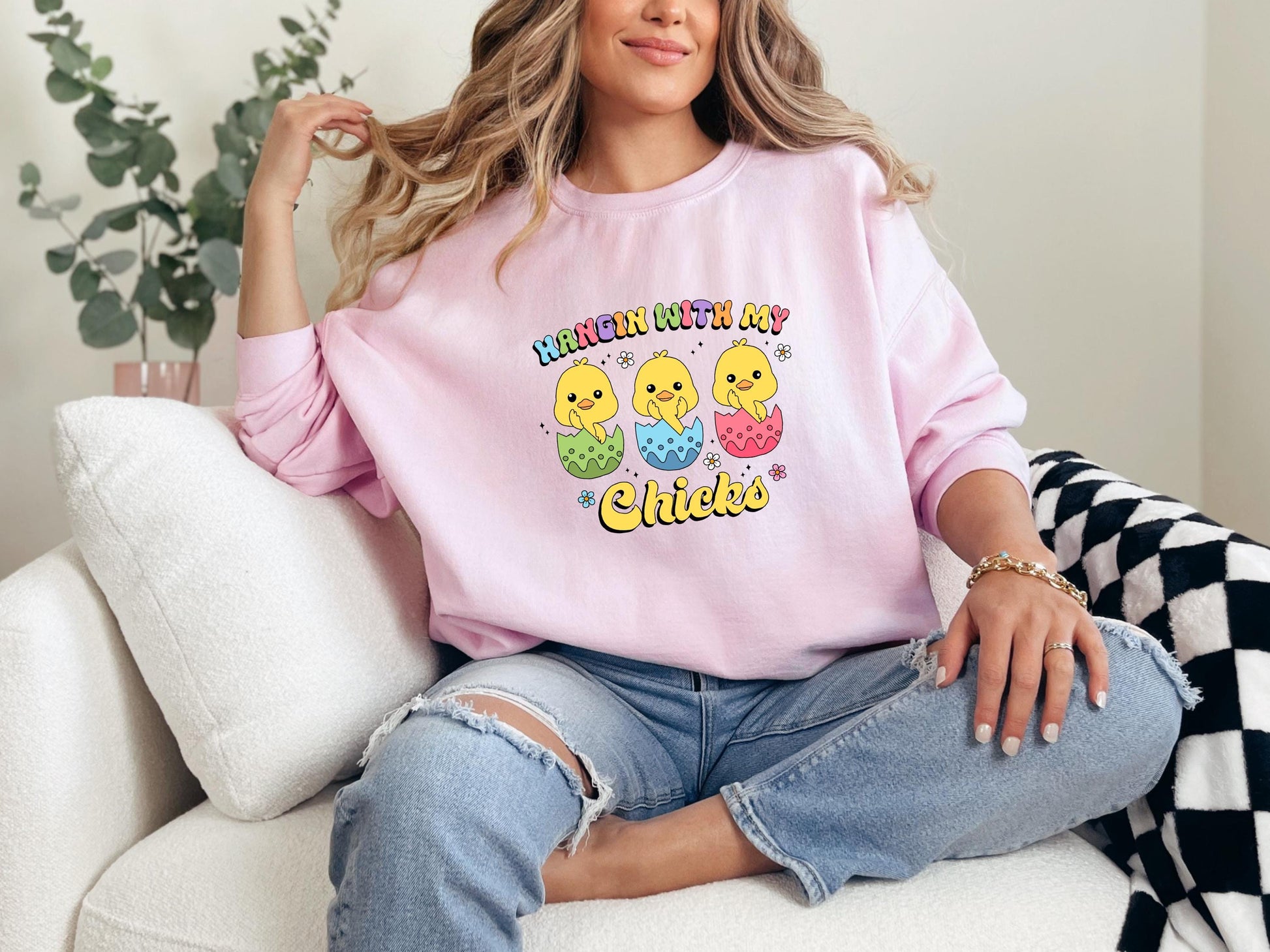 a woman sitting on a couch wearing a pink sweatshirt