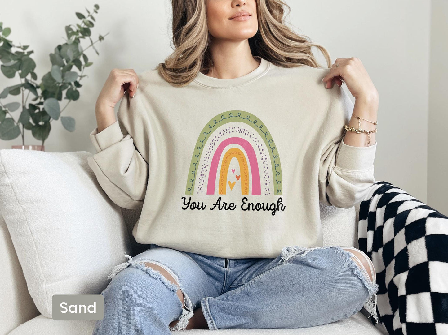 a woman sitting on a couch holding a t - shirt that says you are enough