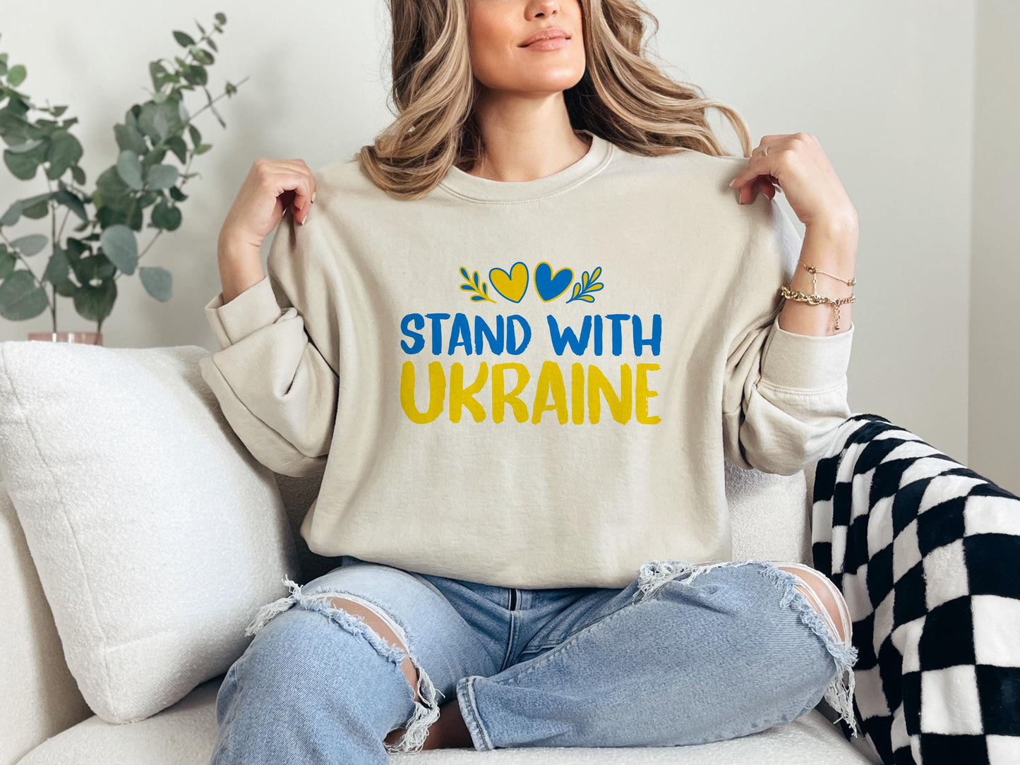 a woman sitting on a couch holding a t - shirt that says stand with ukraine