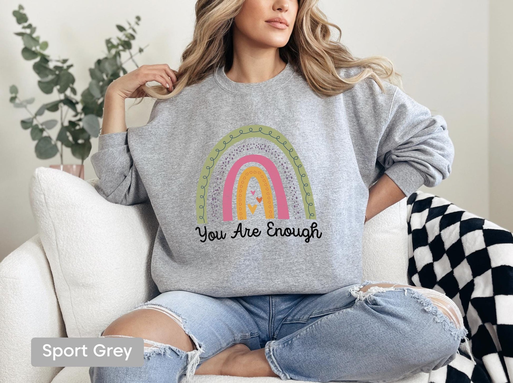 a woman sitting on a couch wearing a sweatshirt that says you are enough
