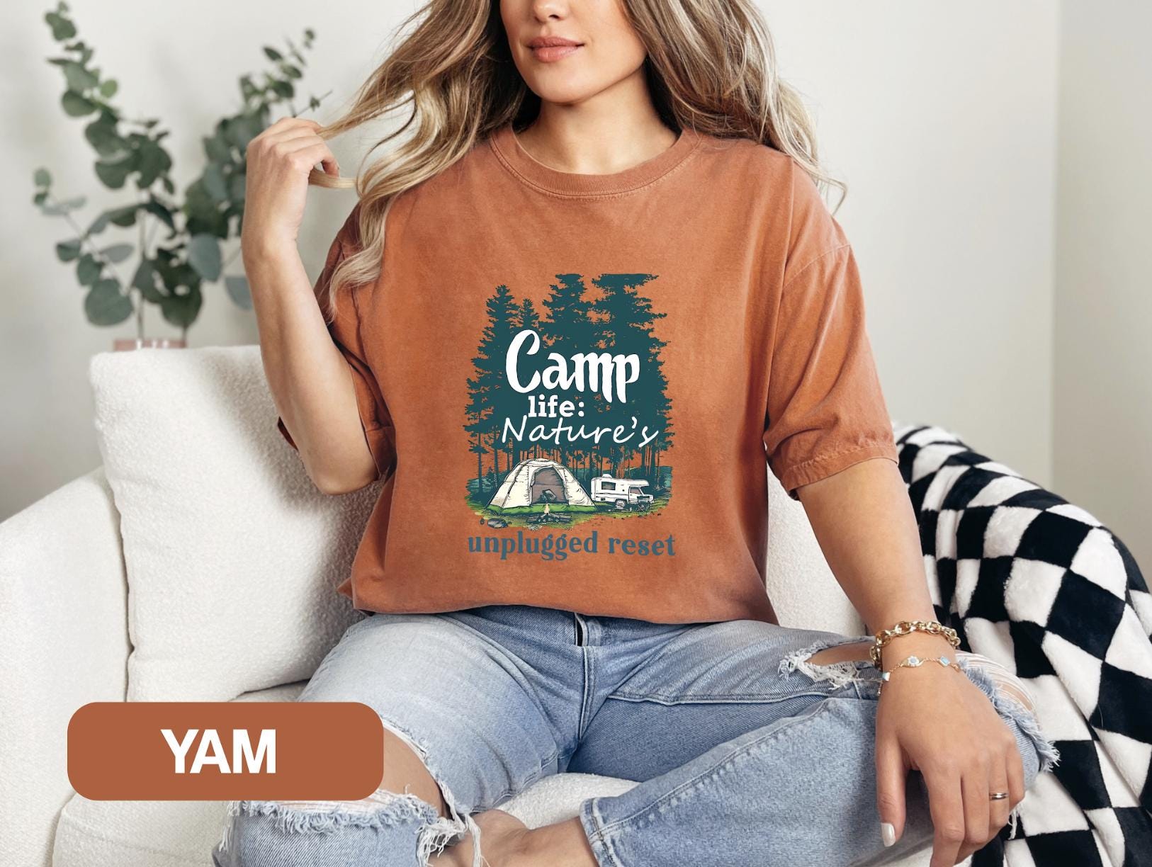 a woman sitting on a couch wearing a camp life nature&#39;s camp t -