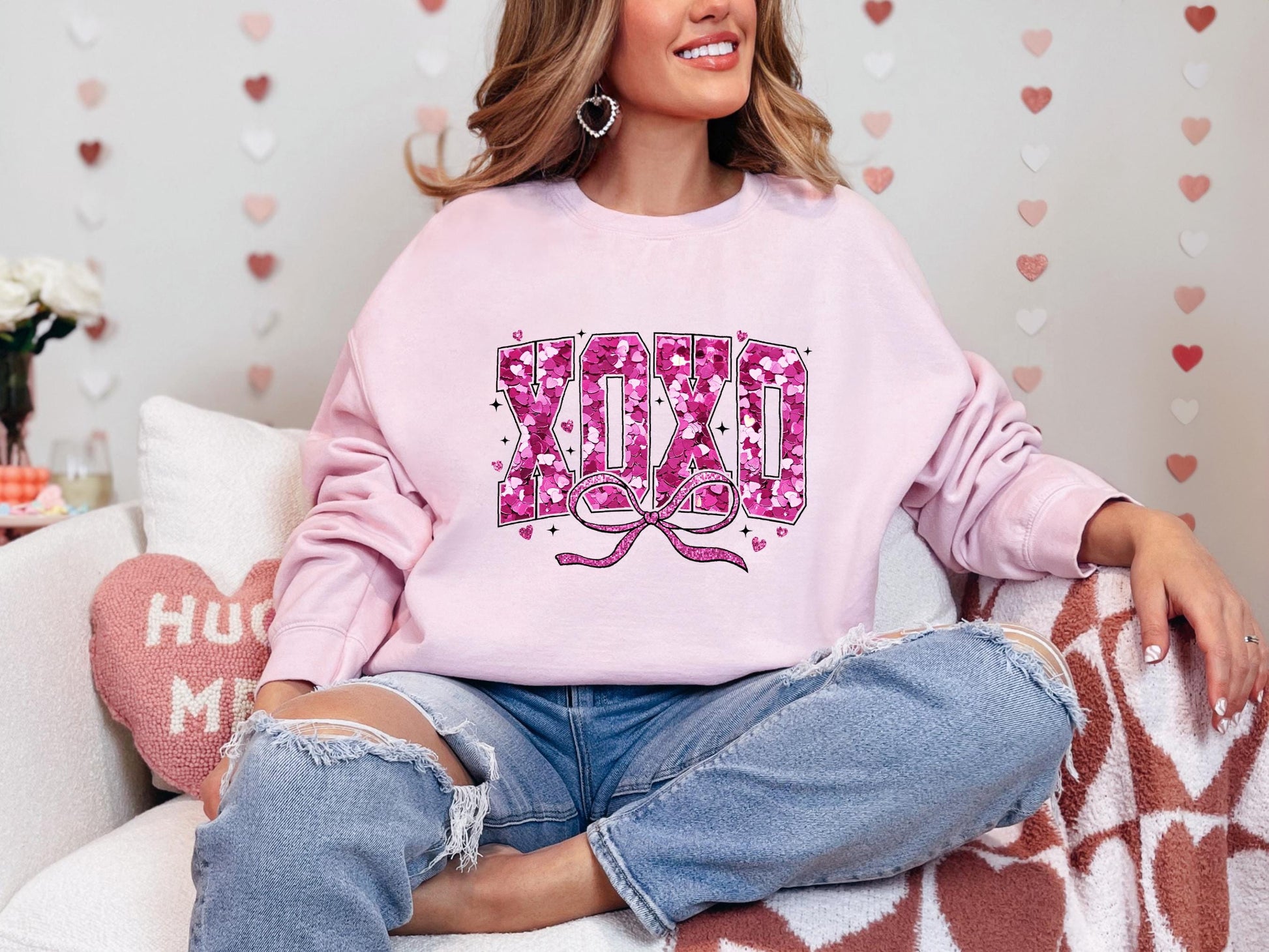 a woman sitting on a couch wearing a pink sweatshirt