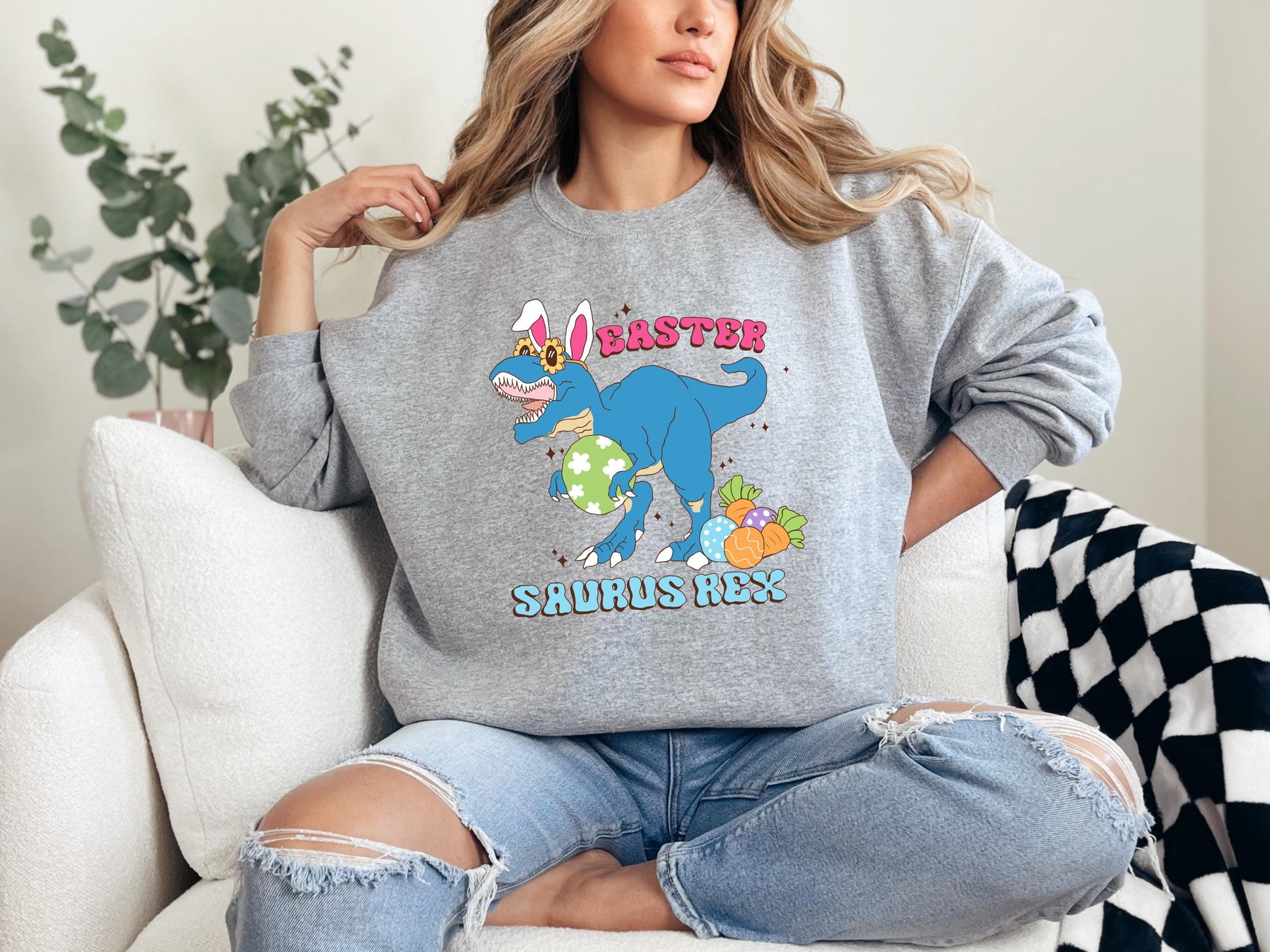 a woman sitting on a couch wearing a sweatshirt with a dinosaur on it