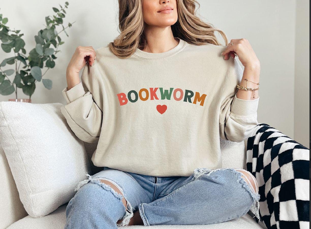 a woman sitting on a couch holding a book worm sweatshirt