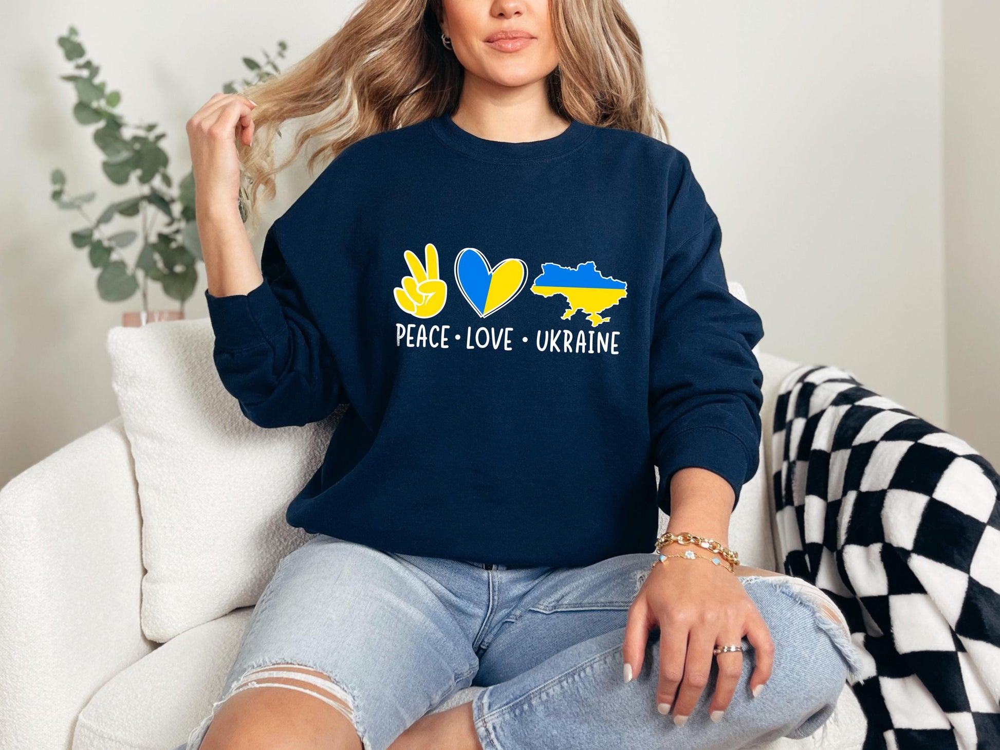a woman sitting on a couch wearing a peace love ukraine sweatshirt