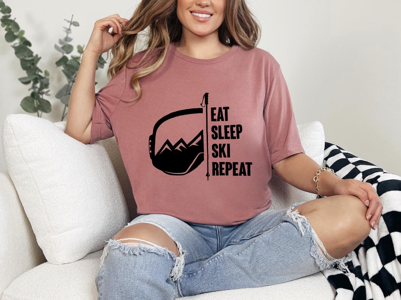 a woman sitting on a couch wearing a t - shirt that says eat sleep ski